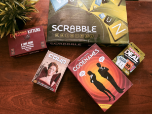 A collection of top board games, including Scrabble, Codenames, Coup, Exploding Kittens, and Monopoly Deal, arranged on a wooden table—perfect picks for an exciting family game night.